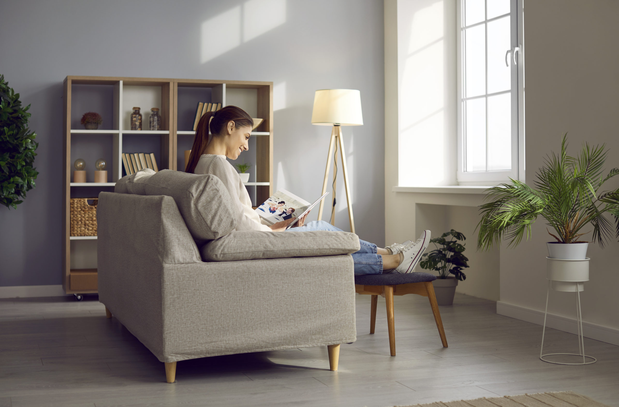 Happy woman looking at pictures in photo book while relaxing on comfortable couch at home